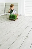 Kind sitzt auf dem Verandaboden und giesst kleines Kräuterbeet