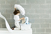 Kind auf Sideboard sitzend vor grauer Steinwand und wirbelt die Wäsche herum