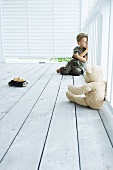 Junge mit Spielsachen sitzt auf Holzboden einer Veranda