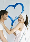 Couple painting, woman drawing heart on wall