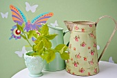 Vintage-style metal jugs against green wallpaper with butterfly motif