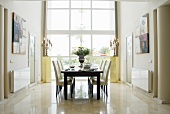 Dunkler Holztisch und weiße gepolsterte Stühle vor raumhohem Fenster in elegantem Ambiente