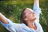 Young woman dancing in spray of garden sprinkler
