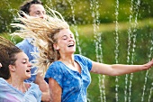 Friends running through sprinkler spray in garden