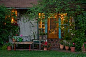 Verwunschenes Sitzplätzchen mit Ziegelstufen zur offenen Terrassentür und Blick in beleuchteten Wohnraum