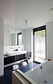Designer bathroom - glass screen on bathtub opposite washstand with trough-style sink against mirrored wall