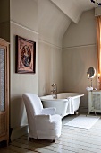 Armchair with loose white cover next to vintage bathtub in simple bathroom with traditional ambiance