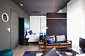 Offener Wohnraum mit grau getönten Wänden und Sitzbank an Raumteiler vor Schlafbereich