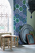 Rustikale Hocker vor schmiedeeisernem Fenstergitter und runde Metalltabletts an Wand mit Fliesenstreifen in orientalischem Muster