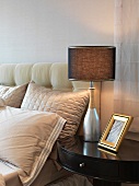 Traditional bedside table with table lamp next to bed with upholstered headboard