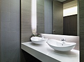 Washbasins on white, slab-like fitted washstand and mirror in minimalist bathroom