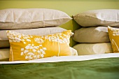 Gelbes Kissen mit modernem Blumenmuster vor Kissenstapel auf Bett