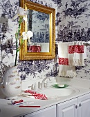 Gilt-framed bathroom mirror hanging over washstand on nostalgic, black and white wallpaper