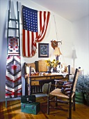 Interior with bureau, chair with woven seat and back, Native American blanket and flag of USA hanging on wall