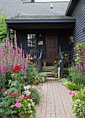 Front door of wooden house surrounded by flourishing flower garden
