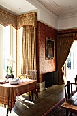 Laid table in front of bay window with floor-length brocade curtains and pelmet in traditional dining room