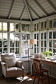 Schlichter Arbeitstisch und Sessel in verglastem Erker mit Sprossenfenstern unter sichtbaren Dachstuhl aus Holz