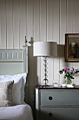 Modern table lamp on traditional bedside table next to bed against white wood panelling