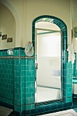 Bathroom with turquoise wall tiles and rounded archway leading to shower