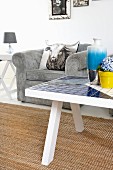 White coffee table with mosaic tiles on sisal rug and pale grey cord armchair with scatter cushion