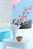 White side table with pink orchid in white vase in front of Japanese floor cushions against light blue wall