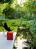 Red cube and butterfly chair on concrete terrace next to small pond