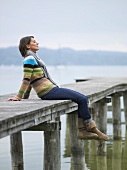 Woman sitting on a wooden jetty on the shore of a lake