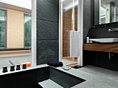 Badezimmer mit steinernen Boden- und Wandfliesen und einer abgesenkten Badewanne