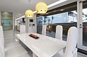 Weisser Esstisch mit Stühlen unter Hängelampen mit gelbem Glasschirm in modernem Wohnraum