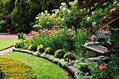 Shady seating area with garden bench in magnificently flowering garden with manicured lawns