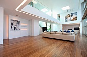 Offener Designer Wohnraum mit heller Polstergarnitur auf Holzfussboden und Blick auf Galerie