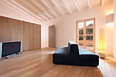 Schwarzes Polstersofa auf Dielenboden im minimalistischen Wohnraum mit weiss getünchter Holzbalkendecke