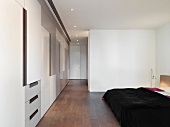 Doppelbett mit schwarzer Tagesdecke und grosszügiger Einbauschrank mit strukturierter Front im modernen Schlafzimmer