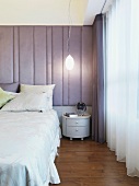 Modernes Schlafzimmer mit Doppelbett und Nachtkästchen vor gepolstertem Wandpaneel