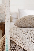 Mit naturfarbenem Garn gestricktes Kissen und Häkeldecken am Holzpfosten eines alten Bettes