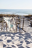 Cloth printed with map motif tied to old wooden post next to wooden walkway leading through sand dunes to sea