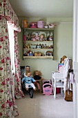 Blick durch offene Kinderzimmertür auf Puppen in Kinderbuggy, Wandregal mit Spielzeug und Schabrackenvorhang mit Rosenmuster wirkt nostalgisch
