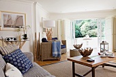 Wicker armchairs, textiles in shades of blue and various accessories made from root wood in open-plan, maritime interior with view of garden