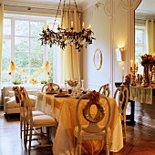 Festively set table below chandelier with lit candles in grand interior