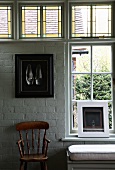 Still-life of framed pictures and simple country-house chair in front of lattice window, stained leaded glass and whitewashed brick wall. Upholstered window seat invites you to linger.