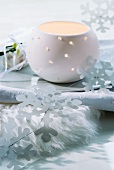Windlicht aus Porzellan und stilisierte Schneeflocken aus Papier auf Schale und Fellunterlage