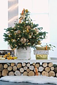 Geschmückter Weihnachtsbaum mit goldenen Kugeln und Geschenke auf Ablage über geschichteten Holzscheiten
