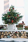 Geschmückter Weihnachtsbaum und Geschenke auf weisser Ablage über geschichteten Holzscheiten