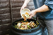 Mann wirft Abfälle in eine Kompost-Tonne