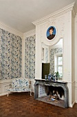 Spiegel und Portrait über dem Kamin in einem eleganten Raum mit blau-weiss gemusterter Tapete