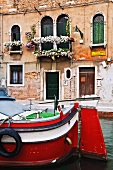Blumengeschmückter, venezianischer Palazzo; davor ein Motorboot auf dem Wasserlauf