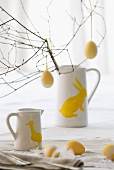 Branches with Easter eggs in white pitchers decorated with bunny rabbits