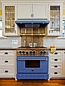 Herd mit blauem Backofen und Dunstabzugshaube in einer Küche mit weissen Schränken