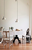 Pendant lamps with aluminium lampshades above set table with black and white curved bases and simple, printed chairs in minimalist period interior