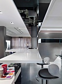 Moderne Küchentheke mit weisser Platte und Designer Barhockern in offenem Wohnraum